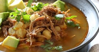 Bowl of pozole rojo with avocado and cilantro for garnish.