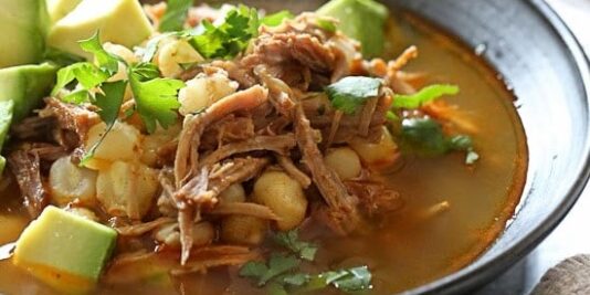 Bowl of pozole rojo with avocado and cilantro for garnish.